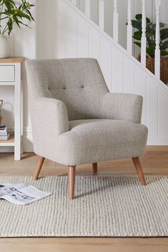 a chair sitting on top of a wooden floor next to a white stair case and potted plant