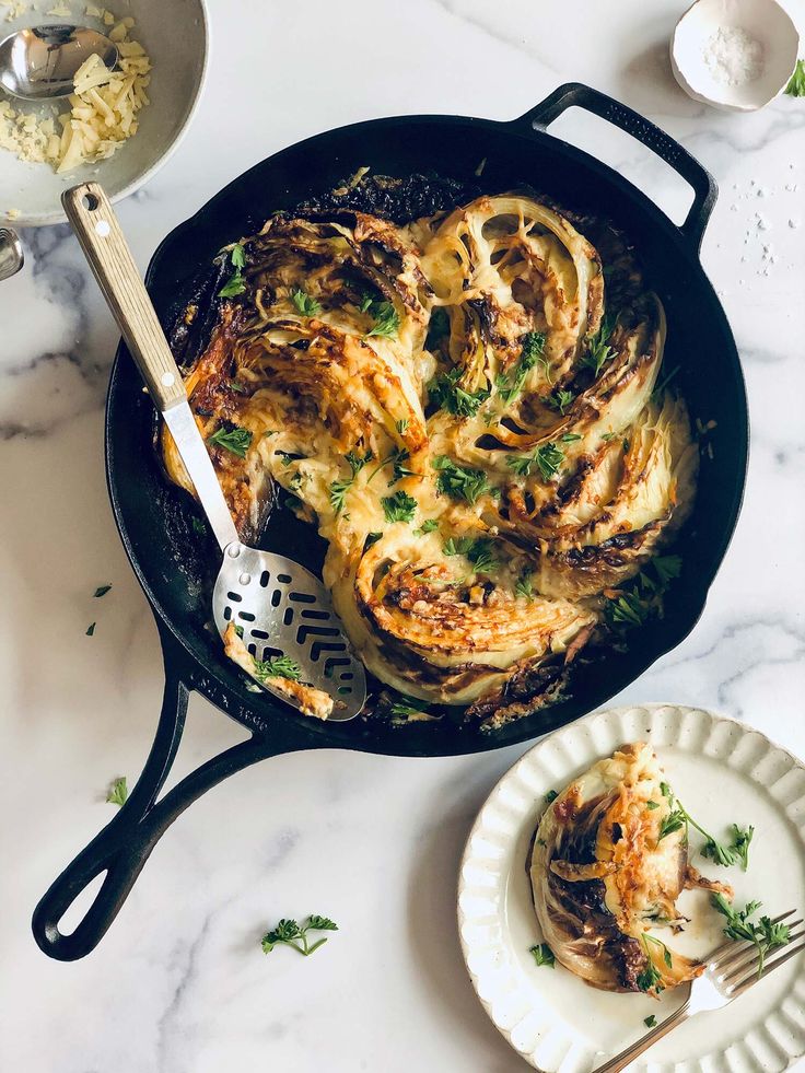 a skillet filled with food on top of a white marble counter next to plates and utensils