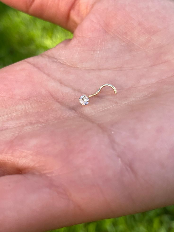 a person's hand holding a tiny white diamond nose ring in their left hand