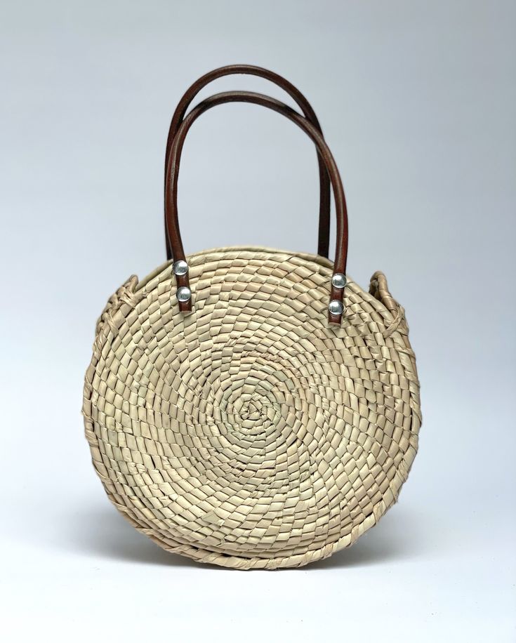 Sustainably Handwoven Straw Circle Bag The Mia Straw Circle Bag is lightweight and durable. This small-size bag will hold all of your essential items. It's the perfect bag for cruising around town. These bags are individually hand-woven with sustainable palm leaves and have naturally tanned leather handles. Thoughtfully designed and ethically made by artisans in Guerrero, Mexico, in a fair trade environment. Each bag is unique and may vary in size, and color, and may have small imperfections. De Natural Woven Leather Top Handle Bag, Top Handle Straw Bag With Woven Leather, Woven Leather Straw Bag With Top Handle, Everyday Woven Leather Jute Shoulder Bag, Beige Straw Bag With Woven Leather And Round Handle, Summer Straw Bag With Woven Leather And Round Handle, Summer Woven Leather Bag With Round Handle, Vacation Shoulder Bag With Woven Leather And Round Handle, Everyday Woven Leather Beach Bag With Double Handle