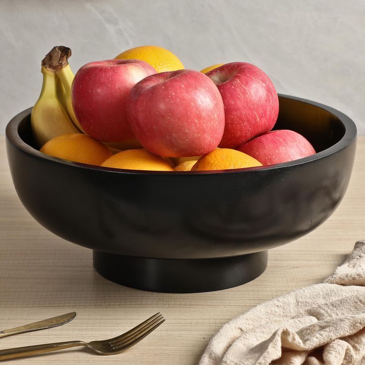 a black bowl filled with apples and oranges next to a knife, fork and napkin