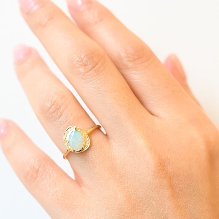 Just gaze into the shimmering opal center of this asymmetric bezel ring and drink in its tranquil beauty. Inspired by shimmering pools found in the desert, this ring features a gemstone cabochon in a golden bezel surrounded by an organic, scattered halo of diamonds. Delicate milgrain beading completes the design with a gentle touch of texture. Made in the U.S.A. 14 karat gold with 8 m x 6 mm opal center and nine round white diamonds totaling 0.045 carat. Yellow Gold Opal Ring With Gemstone Accents, Fine Jewelry Opal Oval Cabochon Ring, Fine Jewelry Opal Ring Oval Cabochon Birthstone, Opal Rings With Gemstone Accents, Yellow Gold Opal Ring With Round Gemstone, Yellow Gold Ring With Ethiopian Opal And Birthstone, Yellow Gold Ethiopian Opal Ring With Birthstone, Yellow Gold Ethiopian Opal Birthstone Ring, Fine Jewelry Opal Ring With Round Stone