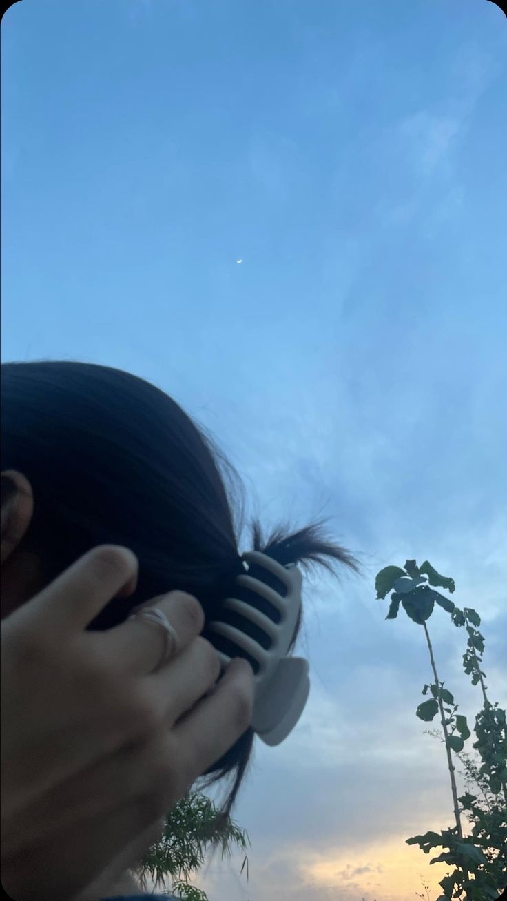 a woman holding a hair brush to her face in front of a blue cloudy sky