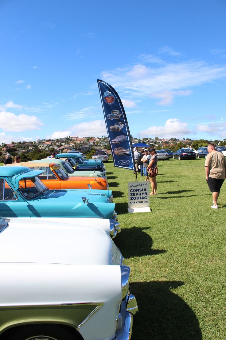 several classic cars are parked on the grass at an auto show, with people walking by