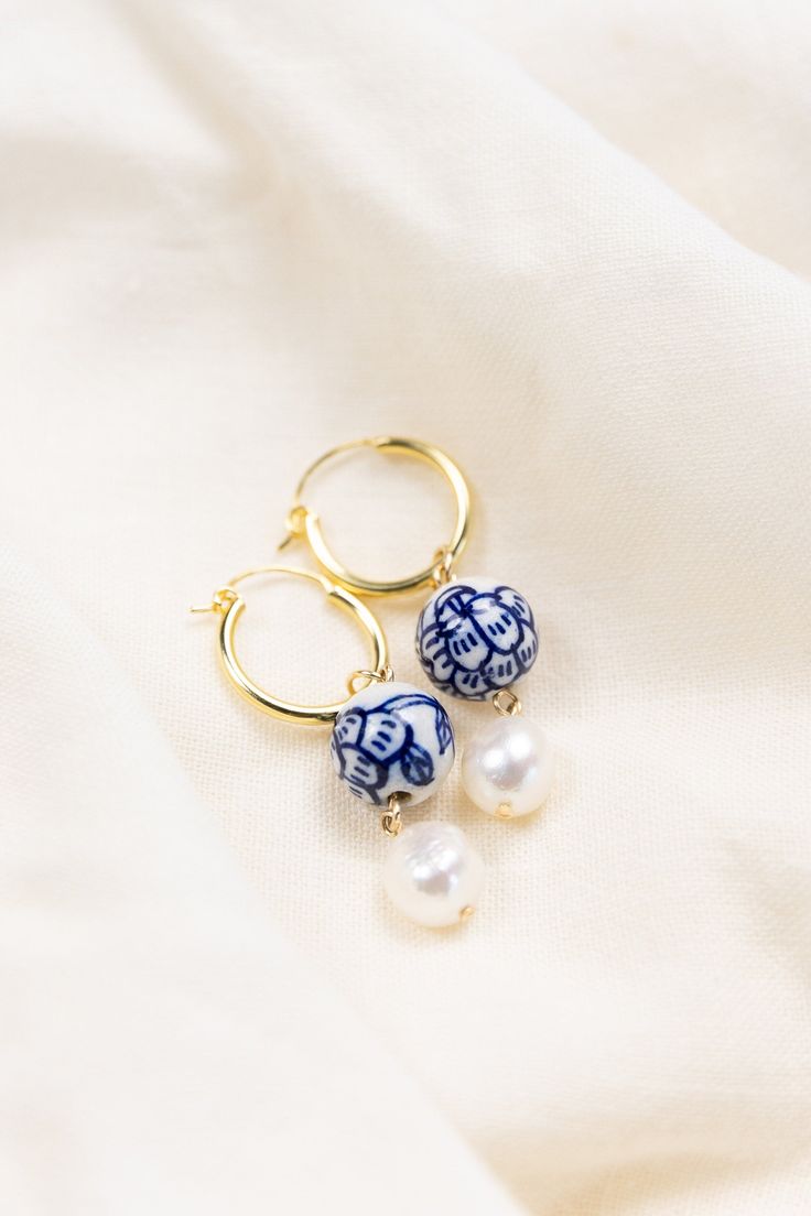 The perfect earrings for colourful jewellery lovers, pottery lovers, or as a traditional pottery gift to celebrate a 9th wedding anniversary! These on-trend hoop earrings feature white ceramic beads with a blue floral pattern, and quality Freshwater baroque pearls. With a contemporary hoop design, these earrings are versatile and perfect for any occasion, whether you're dressing up for a special event or adding a pop of color to your everyday look. Designed to add a touch of fun and sophistication to your outfit, each ceramic bead is meticulously hand-painted, making every pair a work of art.   Material: 925 Sterling silver or gold plated silver, freshwater baroque pearls Dimensions: Earring Hoop: 18mm x 20mm; Drop: 5cm (approximately). Pearl measures approximately 10mm.  Earrings are lovi Blue And Gold Earrings, Pottery Earrings, Blue Earrings Wedding, Colourful Jewellery, 9th Wedding Anniversary, Traditional Pottery, Earring Hoop, Porcelain Earrings, Ceramic Earrings