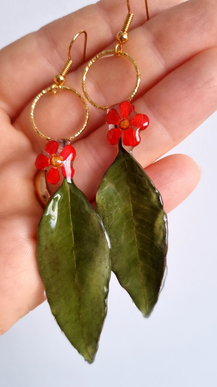 two green leaves with red flowers on them are being held by a person's hand