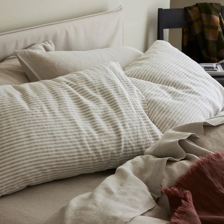 an unmade bed with two pillows and a laptop on the nightstand next to it