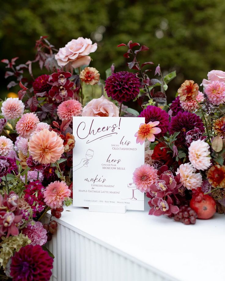 a table topped with lots of flowers next to a white sign that says cheesy