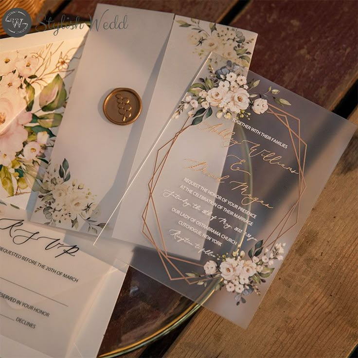 two wedding cards with flowers on them sitting on a table next to some papers and a button