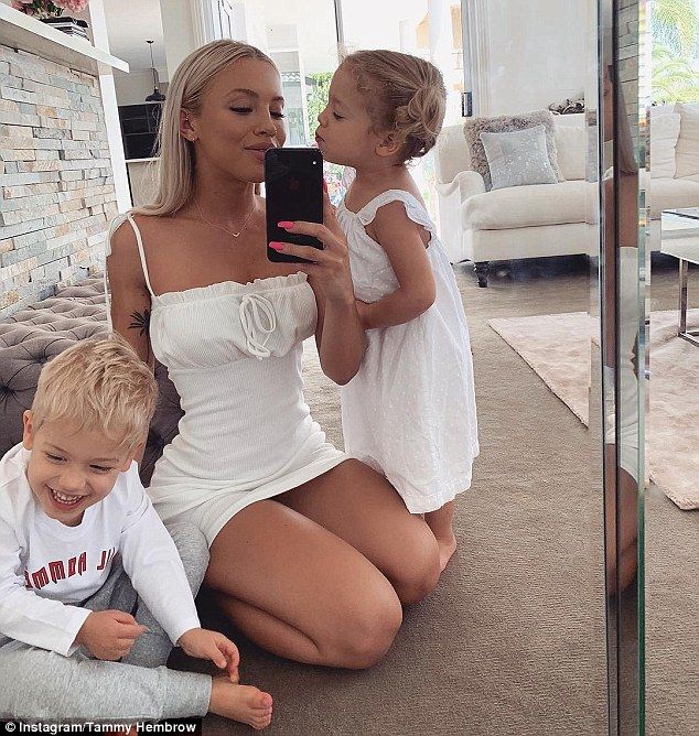 a woman and two children sitting on the floor in front of a mirror looking at a cell phone