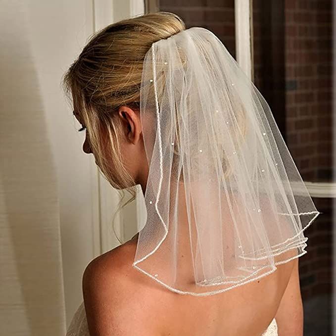 the back of a bride's wedding dress with a veil on her head and shoulder