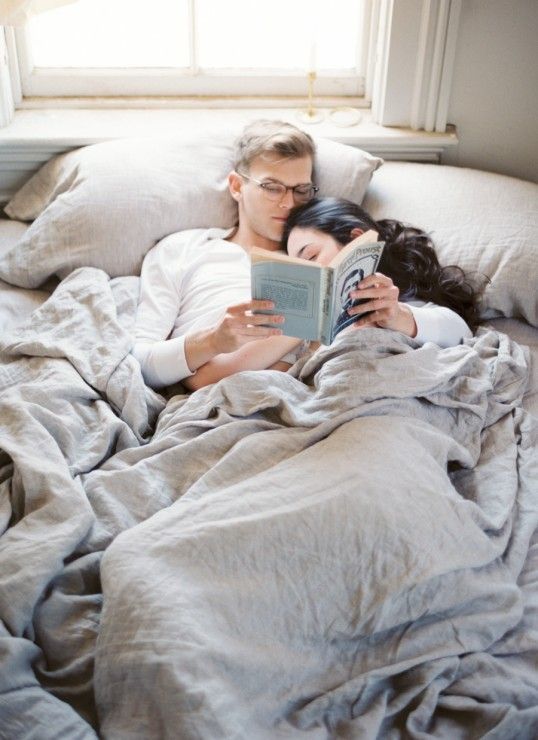 a man and woman laying in bed reading a book