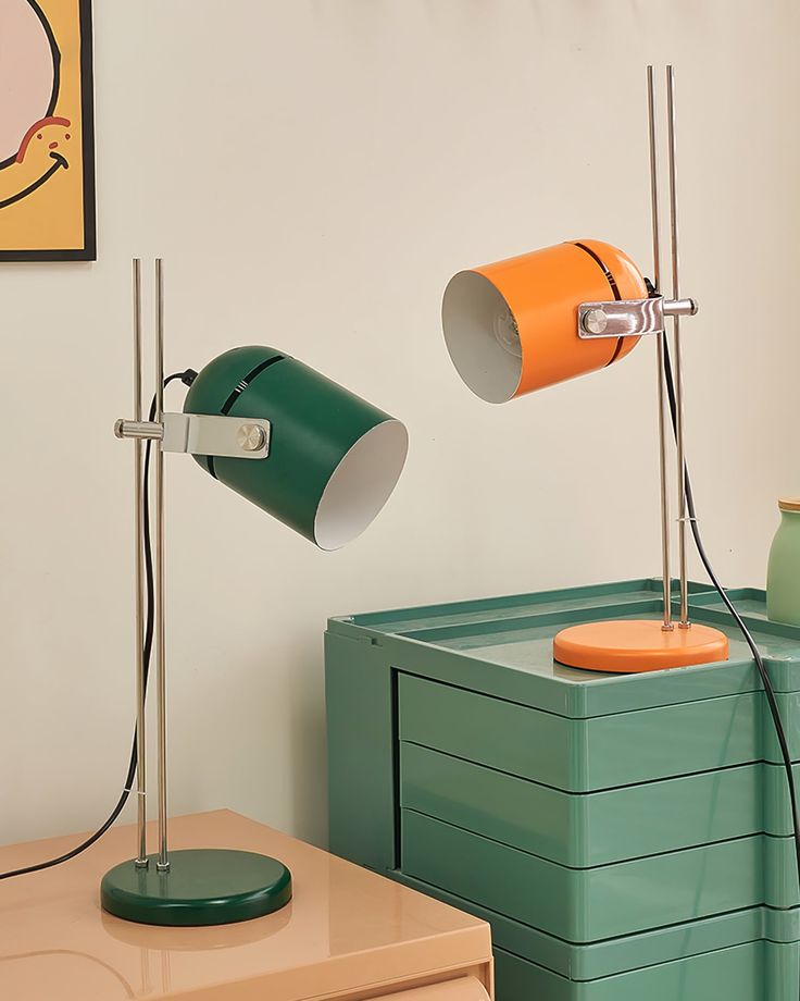 two orange and green lamps sitting on top of a wooden table next to a dresser