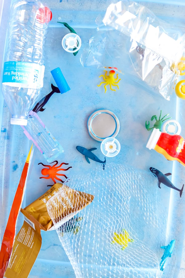 plastic toys and other items are on the table in an ocean themed play tray with clear bags