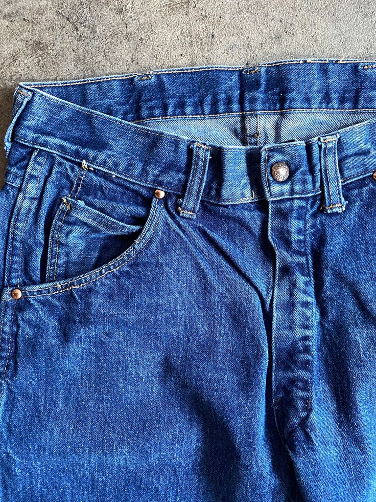 "Excellent 1970s Levi's denim jeans. Featuring the big E on the back pocket tab. Dark wash denim, 100% cotton fiber content. Riveted pockets with unbranded buttons. Overall condition is excellent with no majot flaws. No rips or tears. These jeans have a lot of life left! minimal wear. Please see all photos for details. Refer to measurements below to ensure a proper fit 16.5\" across waist 20\" hip to hip 11\" rise 28\" inseam" Retro Cotton Jeans With Button Closure, Retro Medium Wash Jeans With Patch Pockets, Vintage Dark Wash Bottoms With Patch Pockets, Retro Jeans With Patch Pockets In Medium Wash, Vintage Denim Blue Jeans With Pockets, Vintage Cotton Jeans With Button Closure, Cotton Straight Leg Bottoms With Open Pocket, Vintage Cotton Jeans With Pockets, Retro Denim Jeans With Hip Pockets