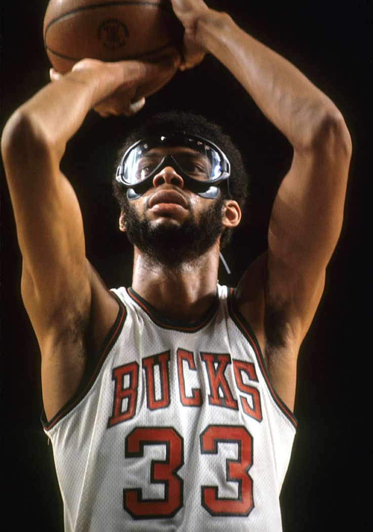 a man holding a basketball in his right hand and wearing goggles on top of his head