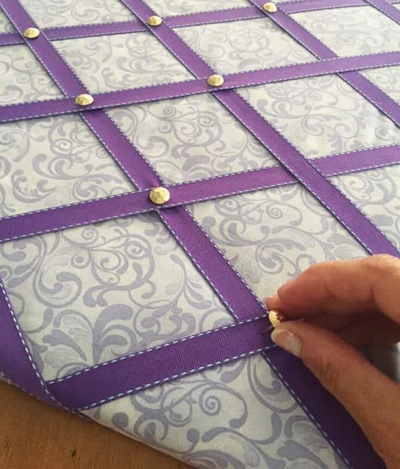 someone is making a quilt with purple and white squares on the front, along with gold buttons