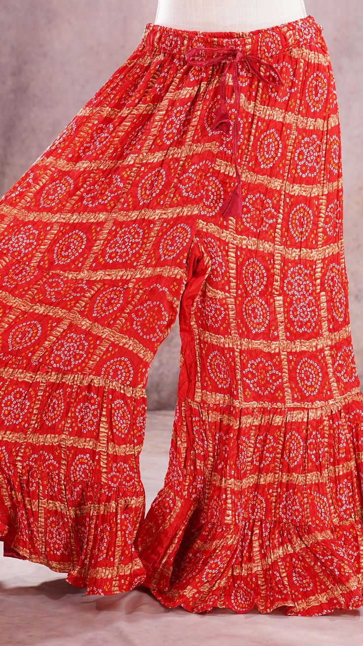 PRODUCT DETAILS These are beautiful Bandhini Palazzos pants that are tiered and have flary hem. The waist has a stretch elastic band with tying strings for a good fit. It is made of paper silk fabric, which has a very good flow. It resembles crushed satin silk. You can wear this with an Indian Kurti or a stylist western top!! Your creativity is the limit with these colorful, printed Palazzo pants! :) Size: One Size Length: 38 inches In seam: 25 inches Waist: expands upto 42 inches Material & Car Red Ruffled Sharara For Diwali, Traditional Tiered Sharara For Festivals, Bohemian Bandhani Print Sharara, Bohemian Fitted Sharara With Bandhani Print, Bohemian Fitted Bandhani Print Sharara, Fitted Bohemian Bandhani Print Sharara, Festive Floor-length Party Bottoms, Anarkali Palazzo Set With Ruffles For Festivals, Traditional Tiered Sharara For Diwali