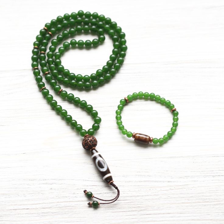 A DharmaShop exclusive design, this bracelet features bold Green Jade beads with a true agate Dzi bead centerpiece and copper spacers. The Dzi bead comes directly from DharmaShop founder, Sander Cohen's personal collection that has accumulated over the last 20 years throughout his travels to Kathmandu and Taiwan. Dzi beads are believed to bring protection and prosperity to the wearer. Each bead is unique, making your bracelet one-of-a-kind. Pair it with the matching Sky Door Dzi Heart Chakra Jad Agate Bracelets With 108 Beads For Meditation, Agate Meditation Bracelets With 108 Beads, Meditation Jade Bracelet With 108 Beads, Jade Gemstone Beaded Bracelets For Meditation, Agate Beaded Bracelets With 108 Beads For Meditation, Spiritual Jade Beads For Meditation, Beaded Jade Bracelet For Meditation, Spiritual Agate Beaded Bracelets With Polished Beads, 8mm Jade Beads For Spiritual Use