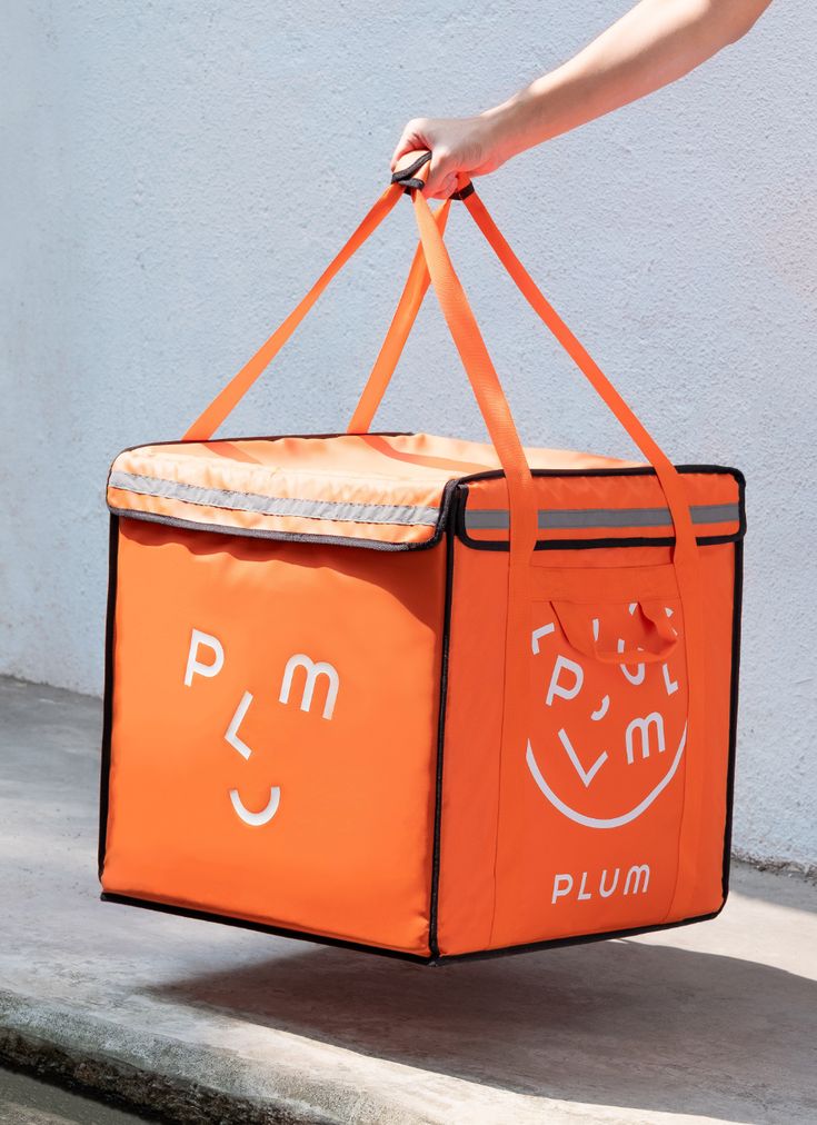 a person holding an orange bag with the word plum printed on it and smiling face