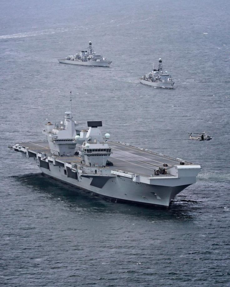 an aircraft carrier in the middle of water with other ships behind it and one boat on the far side