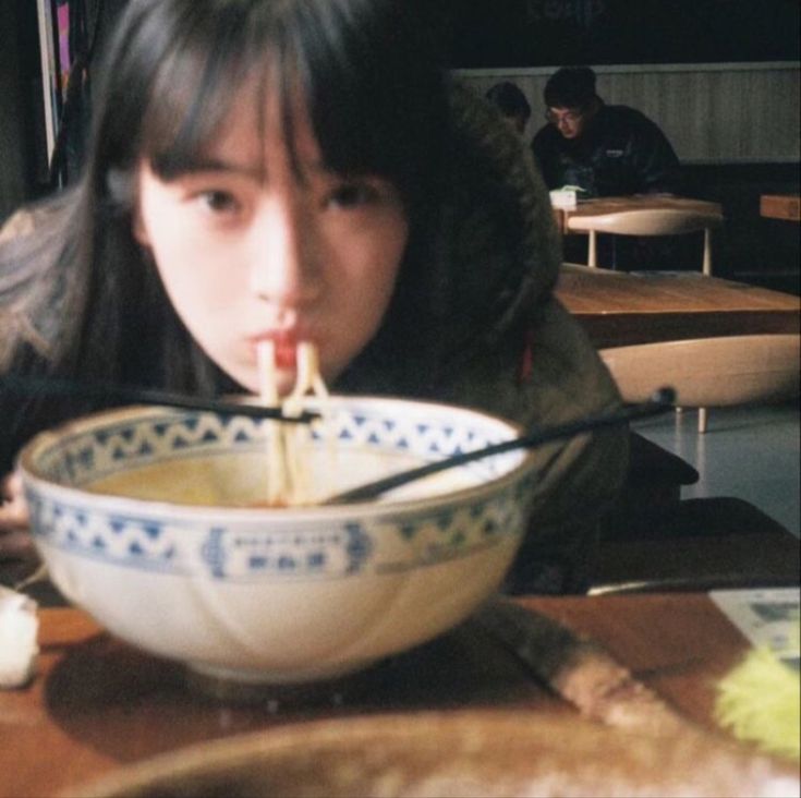 a woman sitting at a table eating food with chopsticks in front of her mouth