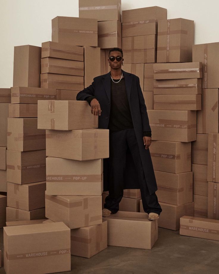 a man standing in front of boxes with his hands on the back of him and wearing sunglasses