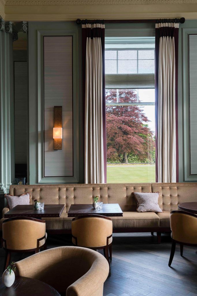 a room with couches, tables and chairs in front of two large windows that look out onto a grassy field