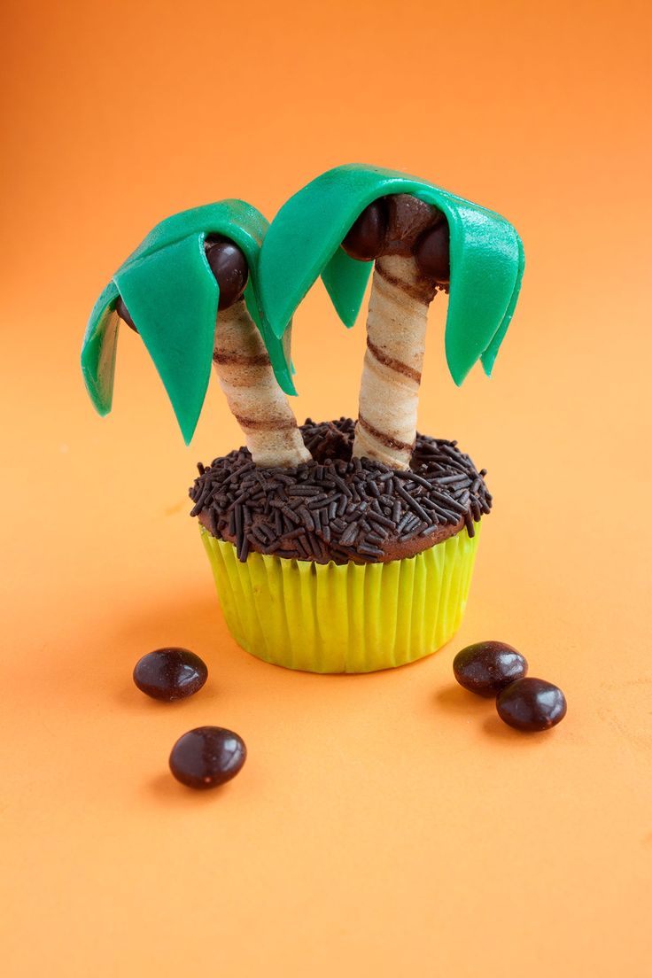 a cupcake decorated with two palm trees and chocolate chips on an orange tablecloth