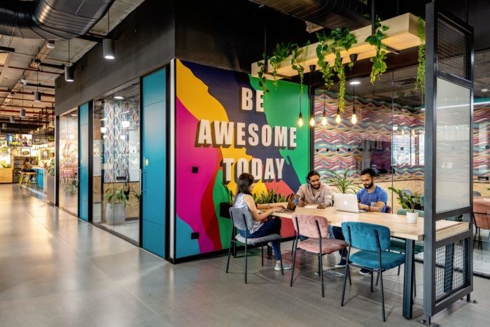 people are sitting at a table in an office with colorful walls and plants hanging from the ceiling