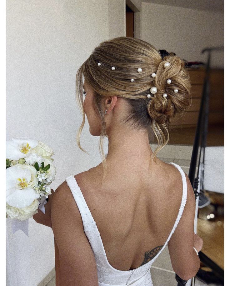 a woman in a white dress holding a bouquet of flowers and looking at the mirror