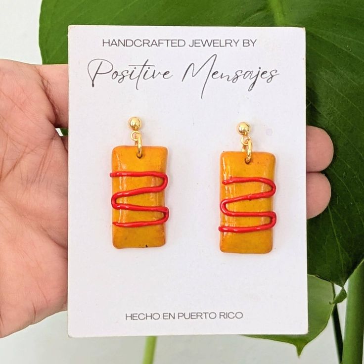 a pair of yellow and red earrings on a card with a plant in the background