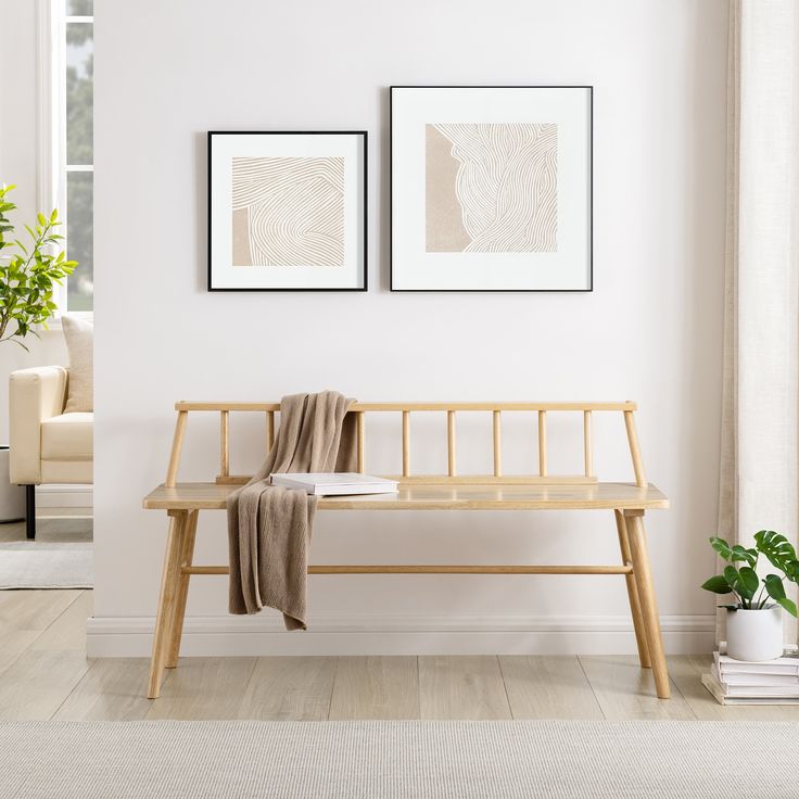 a wooden bench sitting in front of two pictures on the wall next to a plant