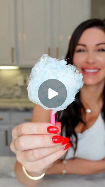 a woman holding up a cotton candy lollipop in her hand and smiling at the camera