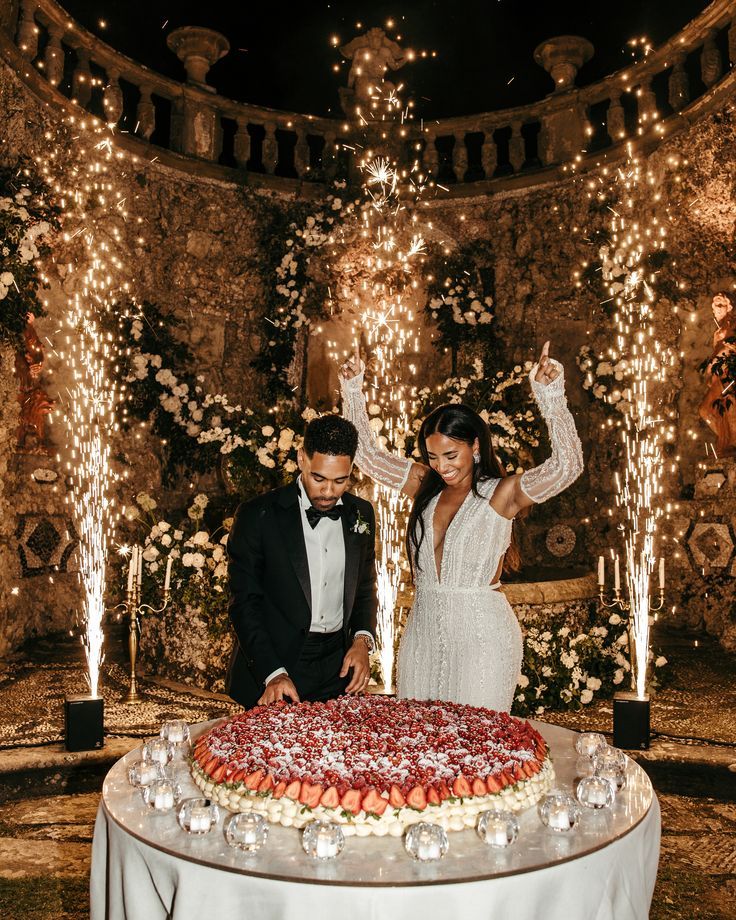 a newly married couple cutting their wedding cake at the reception table with sparklers in the background