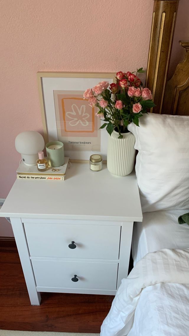 a white nightstand with flowers on it next to a bed