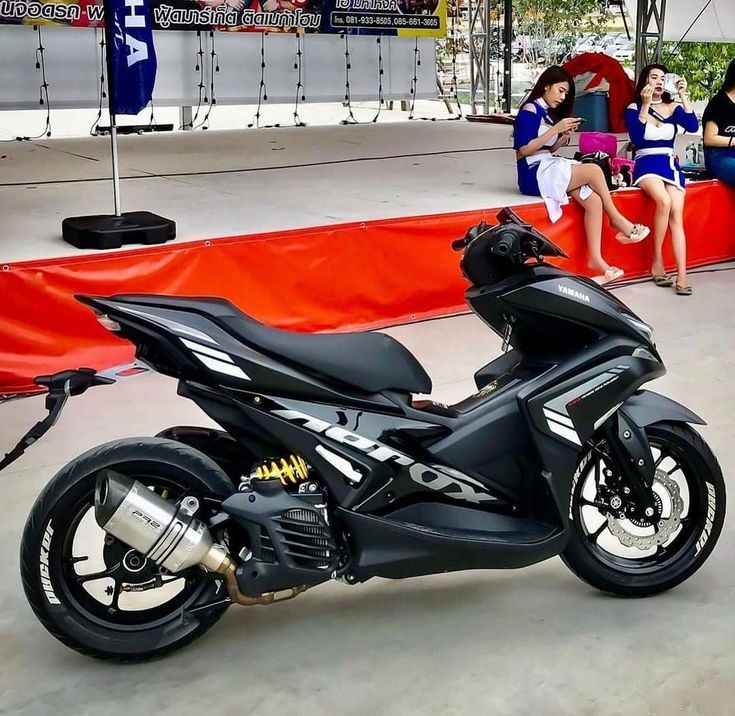 a black motorcycle parked on top of a cement floor next to people sitting in chairs