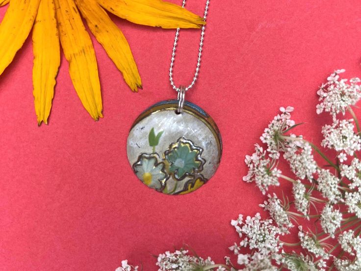 This floral necklace pendant is perfect for a casual or formal look!  Details: The width of the pedant is 1 inch. The necklace drops 1 inch. The ball chain necklace is silver plated, nickel free and has a 9mm lobster clasp. The pendant is made from a vintage tin box and may have scratches that have occurred over time. Thank you for shopping my small business. Please feel free to contact me if you have any questions. All my pieces are made with love. Silver Flower Pendant Necklace With Soldered Detail, Vintage Pendant Necklace With Flower Charm, Bohemian Upcycled Necklaces For Gifts, Vintage Necklaces With Flower Charm Round Pendant, Vintage Necklace With Flower Charm Round Pendant, Vintage Flower-shaped Nickel-free Necklaces, Vintage Necklace With Round Pendant And Flower Charm, Vintage Silver Flower Pendant Necklace, Flower-shaped Soldered Necklaces For Gifts