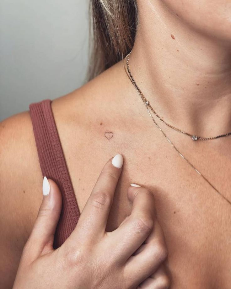 a woman wearing a necklace with a heart on it's chest and holding her hand up to her chest