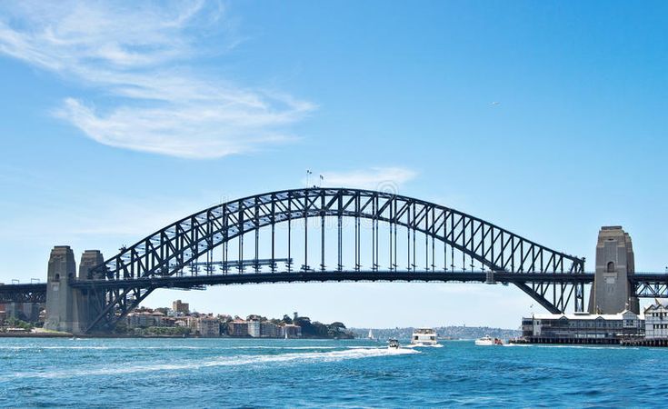 a large bridge spanning over the water with buildings in the background and boats out on the water below