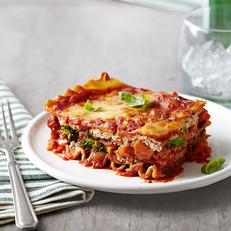 a white plate topped with lasagna next to a fork and glass of water