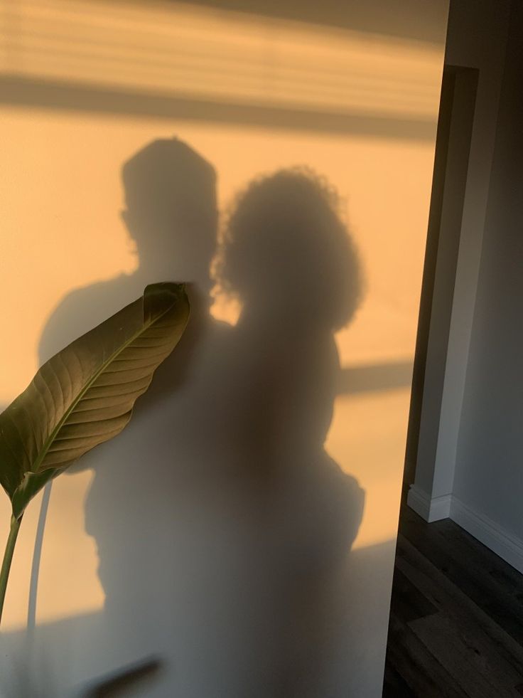 the shadow of two people standing next to a plant