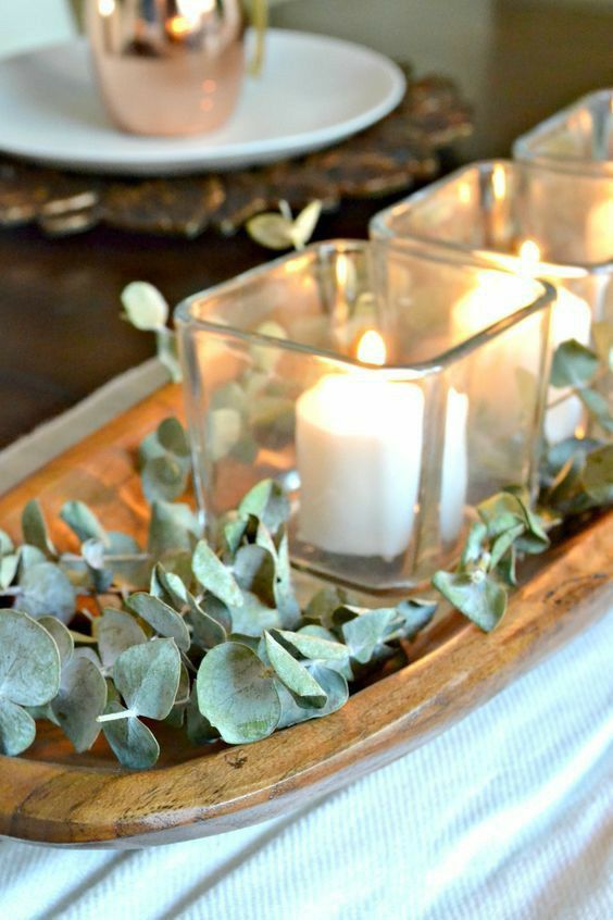 candles are placed in glass containers on a tray with eucalyptus leaves and greenery around them