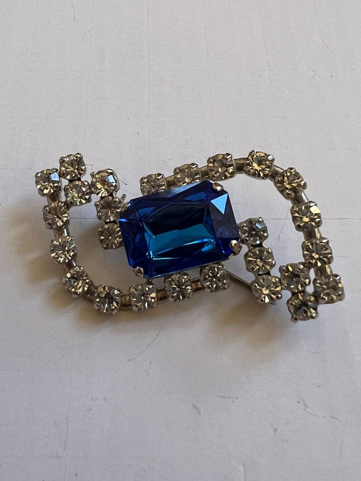 "Elevate your vintage jewelry collection with this stunning Vintage Abstract West Germany Brooch. The blue and clear design exudes a bright and beautiful charm, making it the perfect accessory to add a touch of retro elegance to your sweaters, lapels, scarves, or coats. Stamped West Germany  Approx Measurements 1.75\" Long 1\" Wide Condition: Vintage Excellent.   Sold as is.   PLEASE review all pictures closely.  Contact me with any questions or problems with your order. Thank you for shopping in my store.  International buyers please contact me for shipping details and cost. Most of my items are vintage and used, they will all show some signs of light wear or use.   Major flaws will be noted in the description.  Items are sold \"as is\" so please make sure you look at all pictures careful Classic Blue Brooches For Gifts, Blue Crystal Brooch Jewelry, Blue Crystal Jewelry Brooch, Blue Crystal Jewelry With Brooch Detail, Formal Rhinestone Costume Brooches, Vintage Blue Brooches For Jewelry Making, Vintage Sapphire Brooch Jewelry, Vintage Crystal Brooches For Formal Occasions, Elegant Blue Brooch For Gift