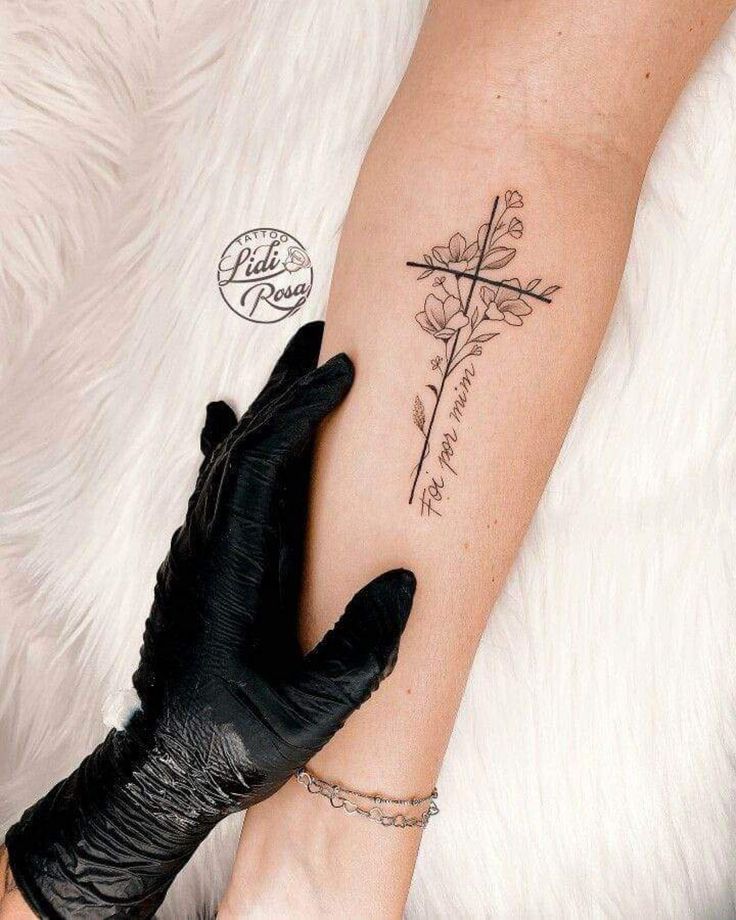 a woman's arm with a cross and flower tattoo on the left side of her arm