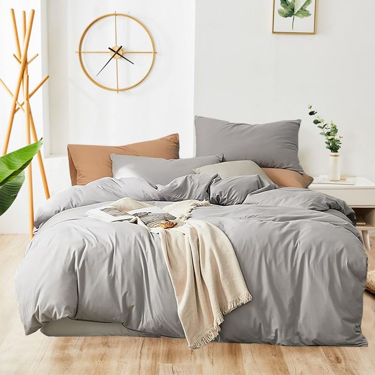 a bed with grey sheets and pillows in a white room next to a wooden floor