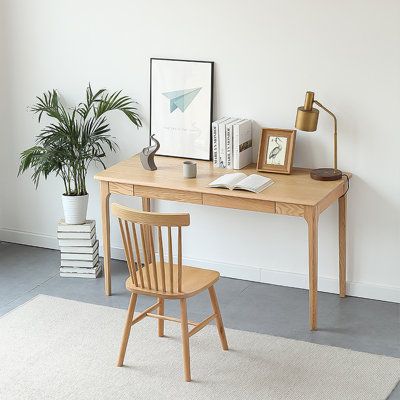 a wooden desk with a chair next to it and a potted plant in the corner