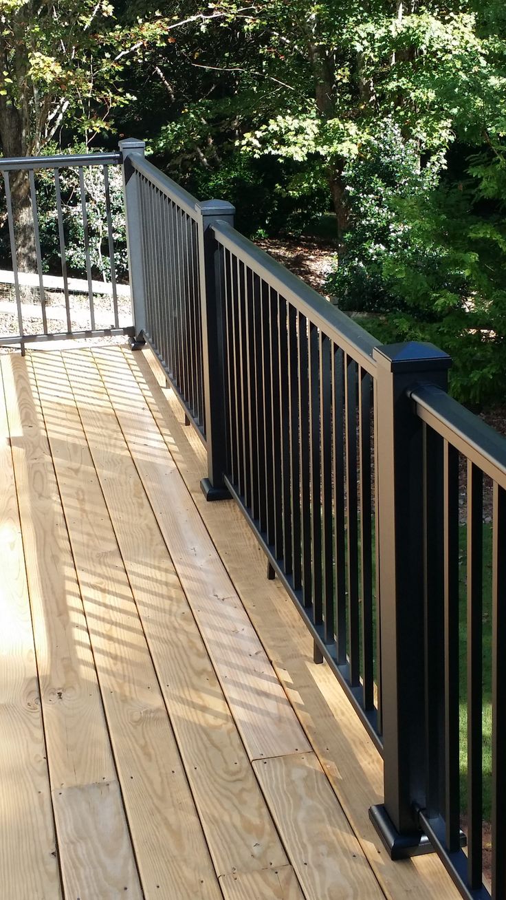 a wooden deck with metal railings and trees in the background