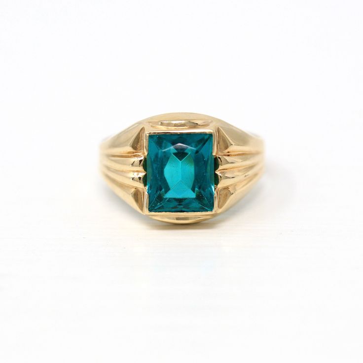 a gold ring with an emerald colored stone in the center, on a white background