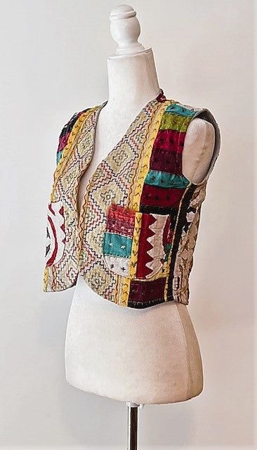 a white mannequin wearing a multicolored vest on top of a dress form